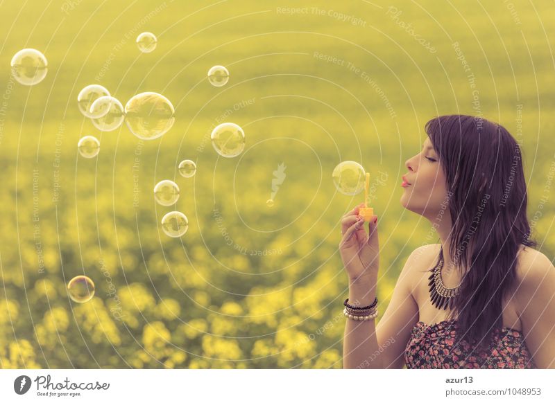 Beautiful young woman blowing soap bubbles in summer on yellow meadow from rapeseed to horizon. Pretty girl with zest for life enjoys the sunshine break and life. Rest and recharge energy from time stress in the environment and nature idyll.