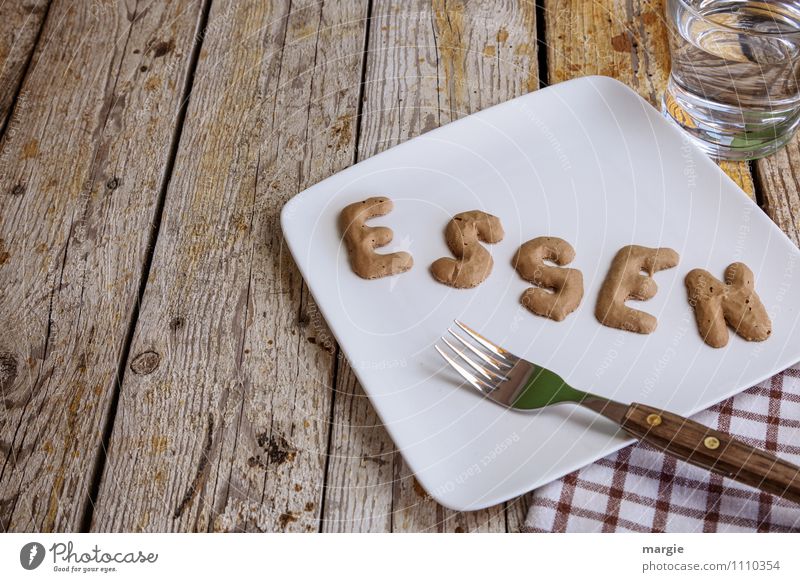 The letters ESSEN on a plate with fork, napkin, a glass of water on a rustic wooden table Nutrition Breakfast Lunch Dinner Picnic Vegetarian diet Diet Fasting