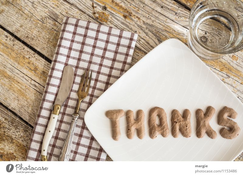 The letters THANKS on a plate with napkin, knife and fork and water glass on a rustic wooden table Nutrition Fast food Finger food Cold drink Drinking water