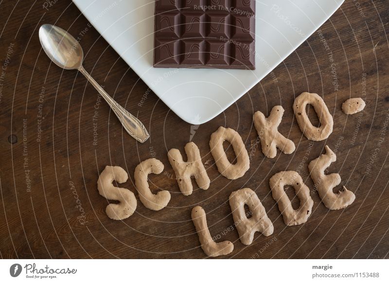 The letters SCHOKOLADE on a rustic wooden table above a plate with a bar of chocolate and a teaspoon Food Dairy Products Dessert Candy Chocolate Nutrition