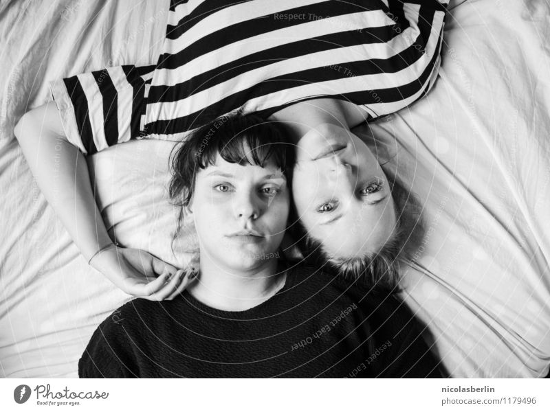 Two young women lie casually together on a bed with heads and look into the camera Couple already Feminine Love Friendship Young woman Harmonious Well-being