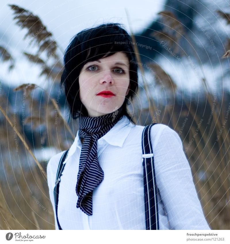 Don't look at me like that. Woman Make-up Wearing makeup Black-haired Fairy tale Suspenders Fir tree Switzerland Common Reed Winter Cold Gray clouds Lake Freeze