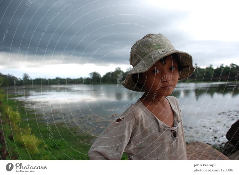 Calm before the storm Child Girl Arm Water Gale Rain Thunder and lightning River Landmark Monument Hat Poverty Curiosity Sadness Longing Cambodia Angkor Wat