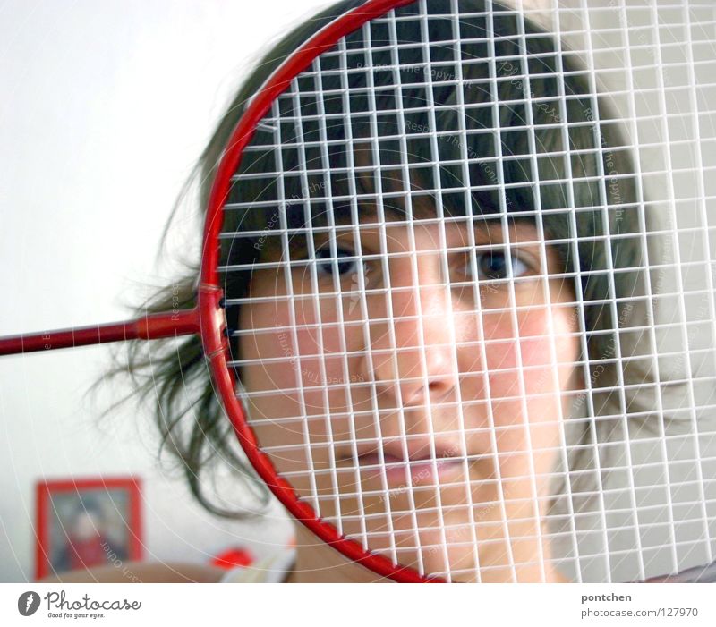 Face of a young woman hiding behind a featherball bat. Repeating the colour red. Sports grouch. Unsportsmanlike. Defense badminton rackets Sports equipment