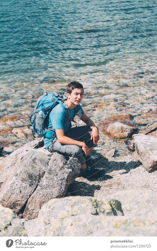 Young boy with backpack sitting on rock over a river - a Royalty