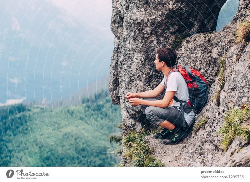 Boy sitting on the rocks in the mountains and looking at a valley