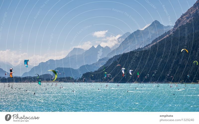 Mountain landscape with a lot of kite surfers and windsurfers moving in a lake. They use the wind to move their boards on the water. Mountains are as background in a sunny day.