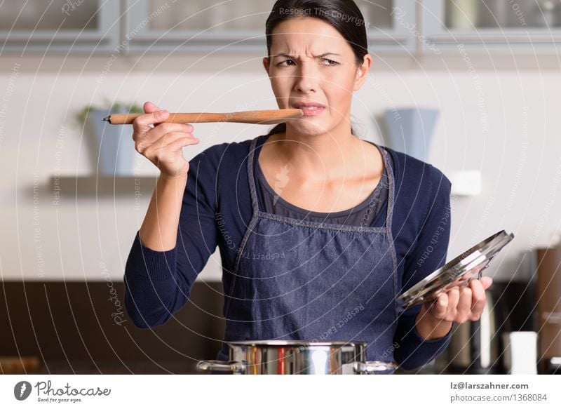 Young cook tasting her food with a grimace Dinner Pot Spoon Face Kitchen Cook Woman Adults 1 Human being 30 - 45 years Hot Anger Food attractive Cooking dislike