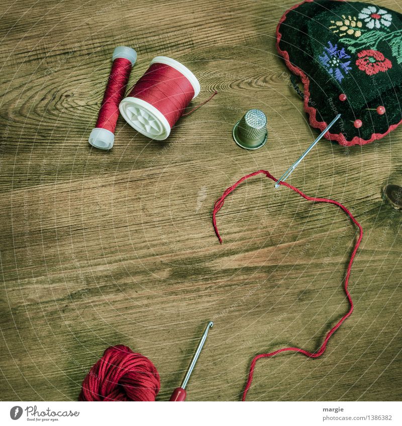 Threaded in red: Sewing equipment, such as needle, thread, thimble wool, crochet hook and a needle cushion on a wooden table Leisure and hobbies Handcrafts Knit