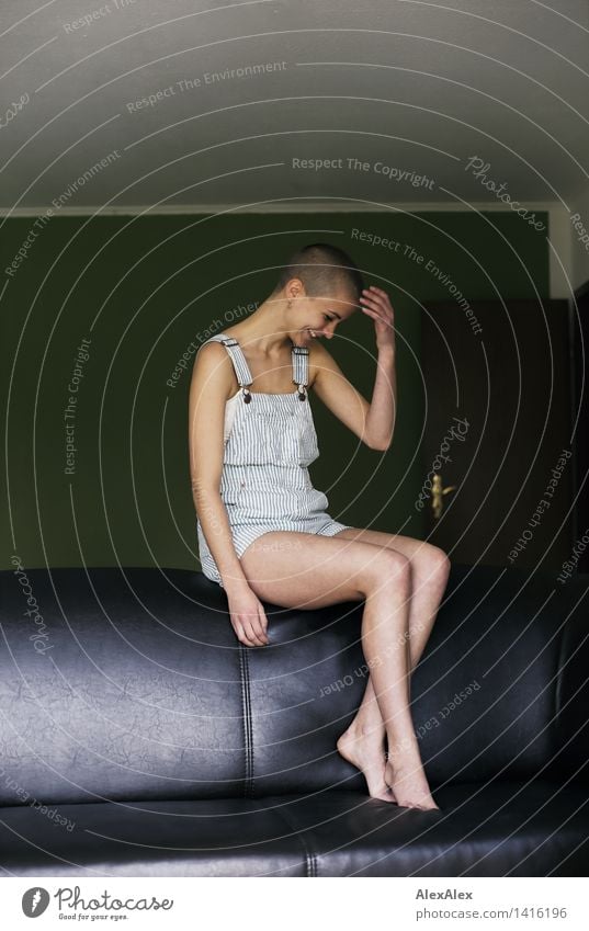 young woman with very short hair sits barefoot on back of couch and laughs Life Harmonious Young woman Youth (Young adults) Legs 18 - 30 years Adults Sofa