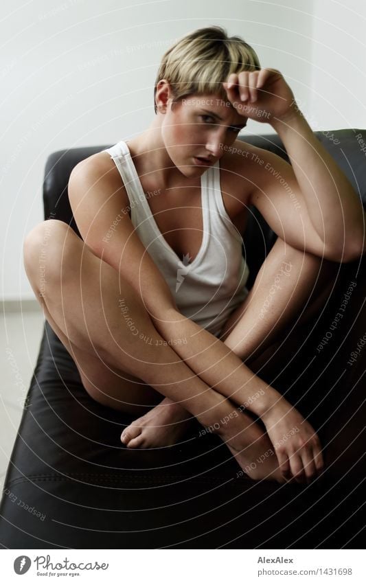 Young woman with long brunette hair and long legs sits on bed in