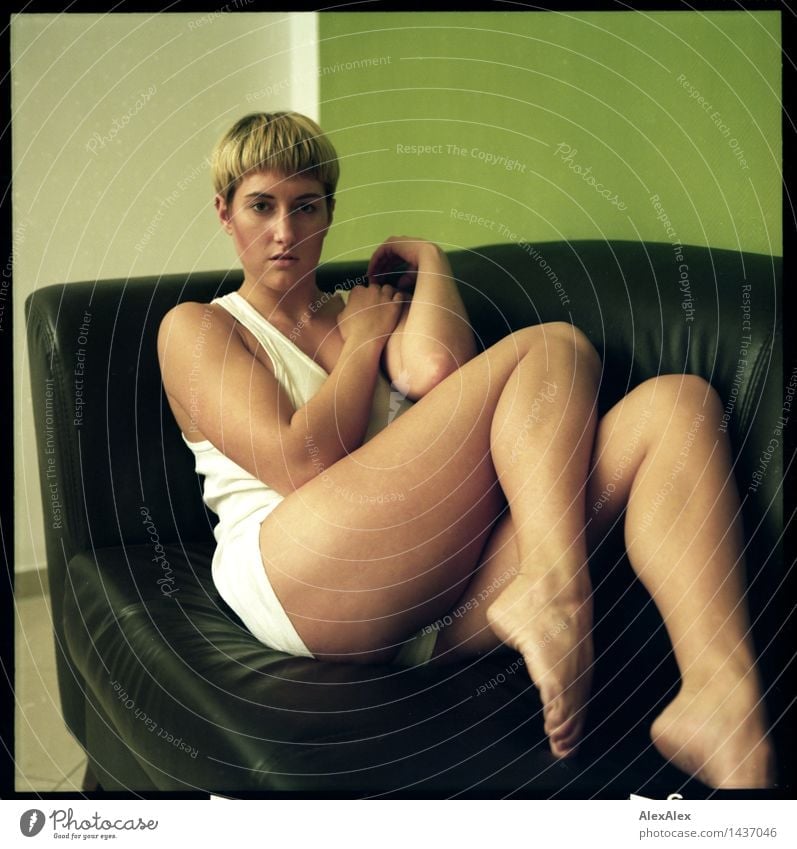 Analog image (6x6) of young woman sitting barefoot in underwear on dark couch and putting on legs Style Well-being Relaxation Room Sofa Young woman