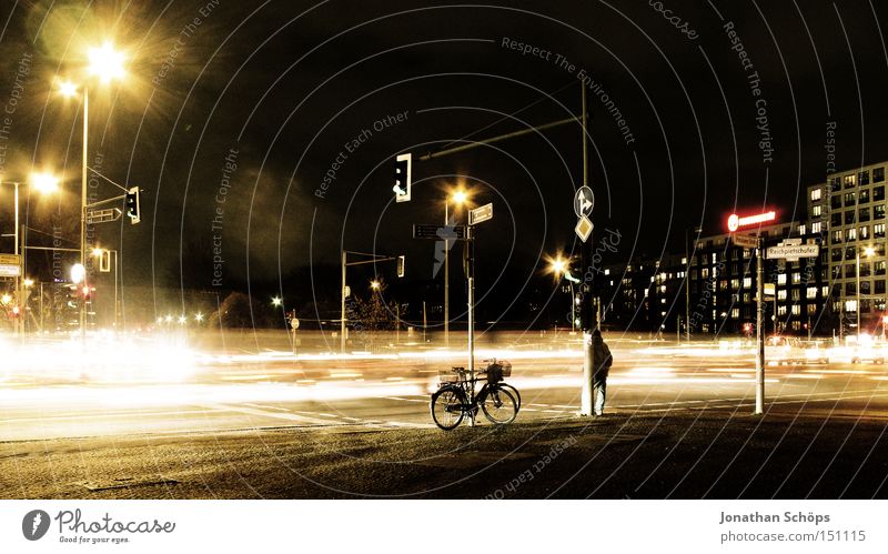 Man stands next to bicycle at night at Berlin crossroads with traffic Town Transport Traffic infrastructure Street Crossroads Road junction Traffic light Car