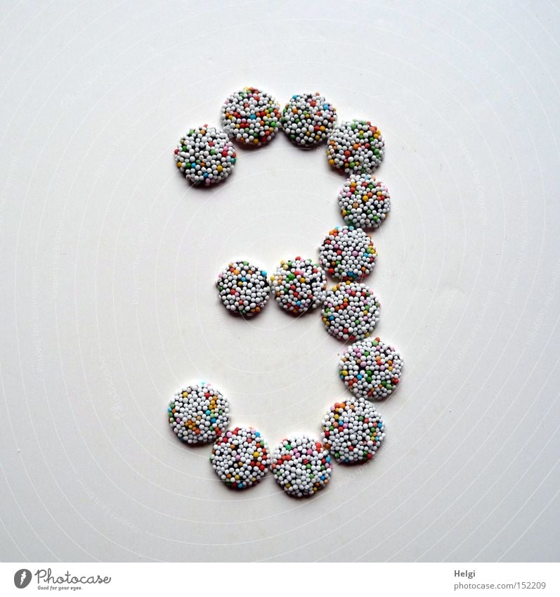 Number 3 laid out of small chocolate candies with colored sugar sprinkles on white background Digits and numbers Advent Calendar Candy Chocolate Granules