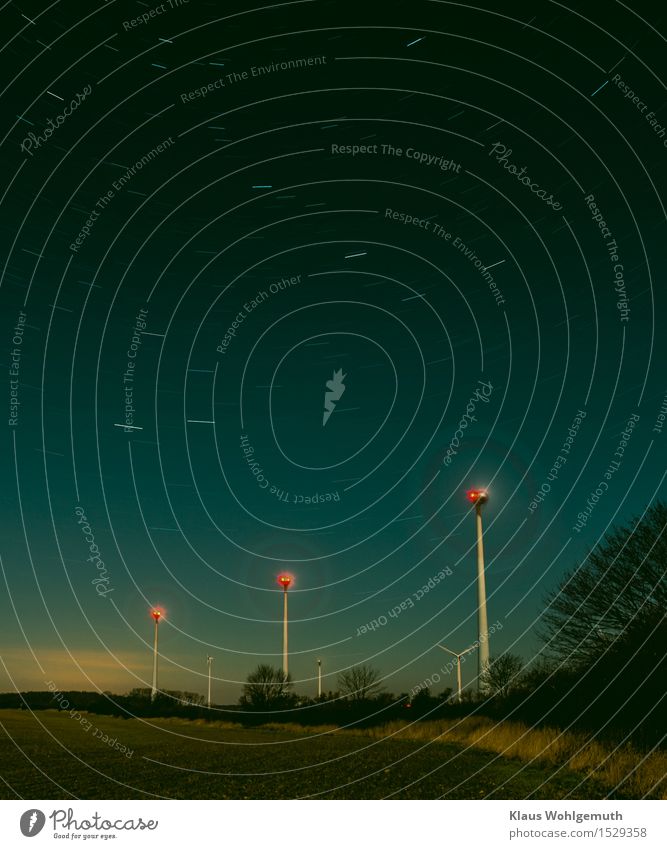 Starry sky over a field with windbreak hedge, in the background wind turbines. The moon shines on the landscape. Night sky Starlit stars in the night sky