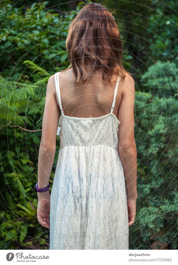 Curious, a girl in a white summer dress looks at green bushes. Joy Contentment Summer Edge of the forest Feminine Girl Back 1 Human being 8 - 13 years Child