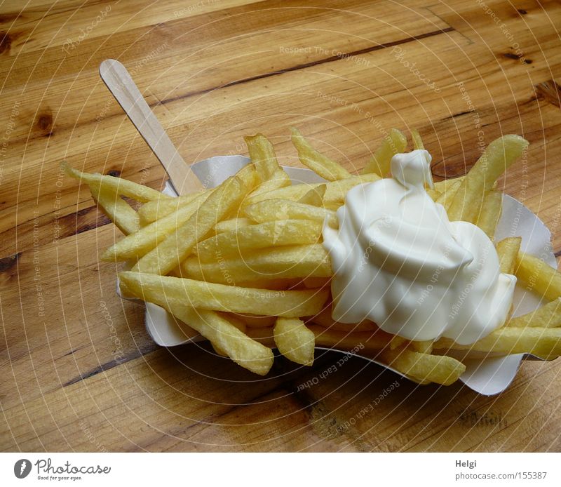 portion of French fries with mayonnaise in a cardboard bowl and a wooden fork on a wooden table Colour photo Exterior shot Copy Space top Food Nutrition