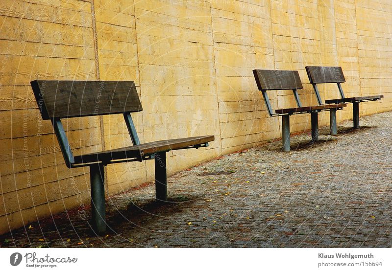 3 benches on paved surface in front of a yellow concrete wall Bench Wall (building) Calm Shadow Loneliness Useless Cobblestones Sidewalk Park