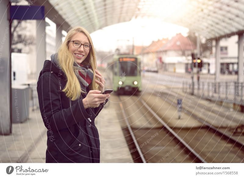 Smiling young woman in black coat, blond hair and eyeglasses standing at station Happy Vacation & Travel Winter Telephone Woman Adults Transport Railroad Blonde