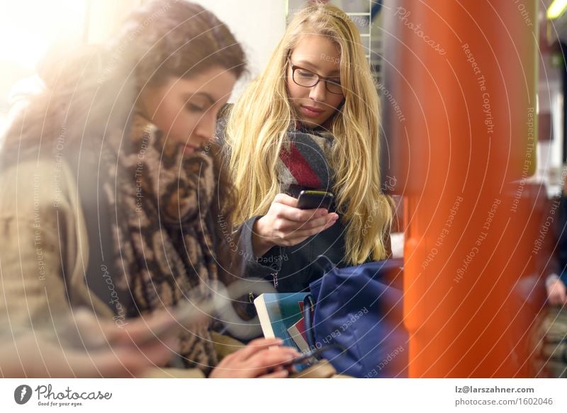 Two young women sitting on commuter train Reading Telephone PDA Technology Woman Adults Friendship 2 Human being 18 - 30 years Youth (Young adults) Scarf