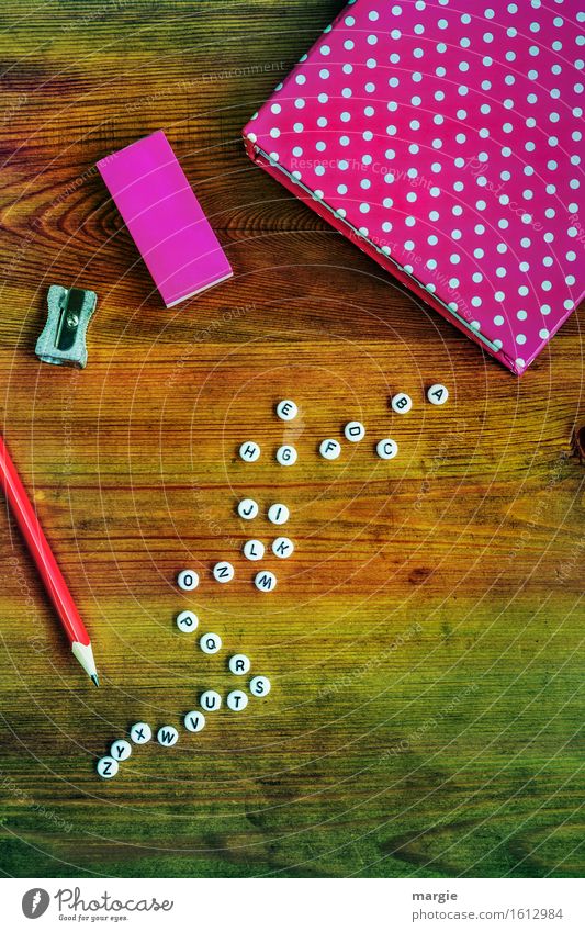Alphabet with white letters, a notebook and eraser in pink, a red pencil and a sharpener on a wooden table Leisure and hobbies Education School Study