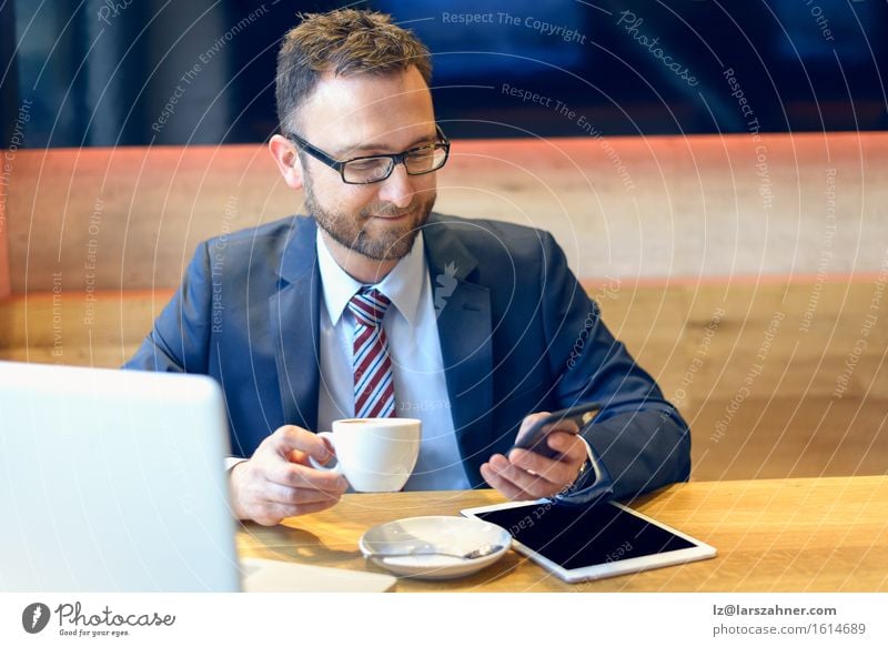 Businessman enjoying coffee and checking his mobile phone for messages with a smile with his laptop and tablet open on the table Coffee Face Work and employment