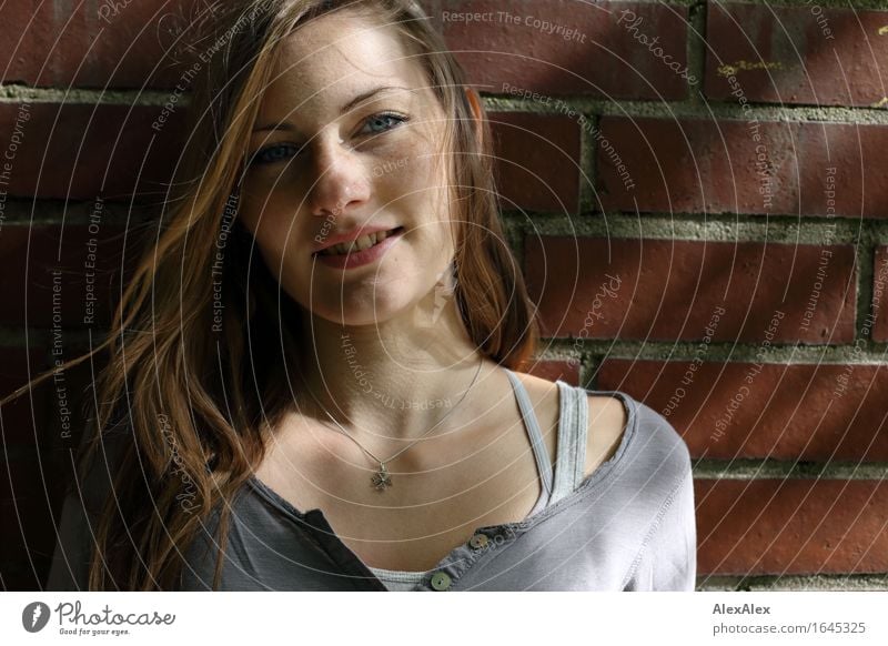 young woman stands in front of a brick wall and smiles - with light and shadow play Hair and hairstyles Face Wall (barrier) Young woman Youth (Young adults)
