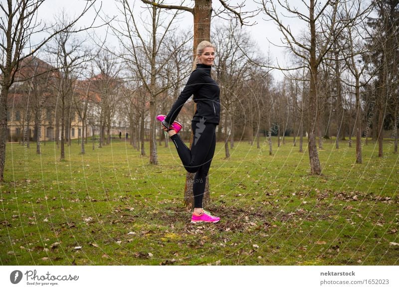 woman stretching right leg in park Lifestyle Body Wellness Calm Winter Sports Human being Woman Adults Tree Park Fitness Smiling Stand Athletic Thin