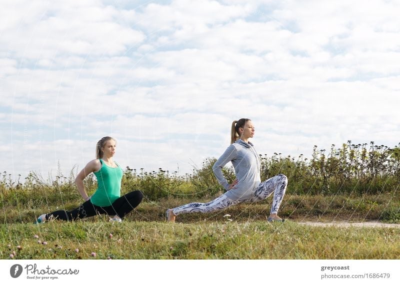 Two attractive athletic young girls exercising outdoors in the countryside doing stretching exercises to stay fit and tone their muscles Lifestyle Joy Beautiful