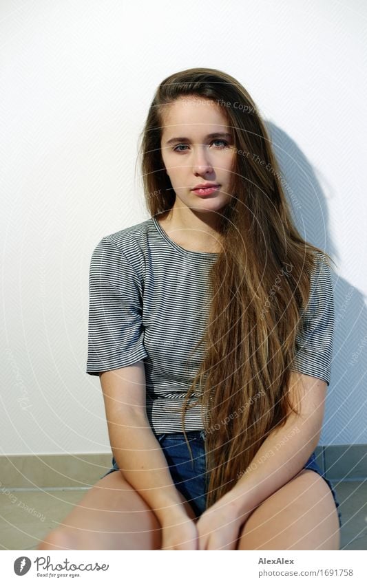 Young beautiful woman with long dark blonde hair sits against a white wall and looks into the camera Style Young woman Youth (Young adults) Hair and hairstyles