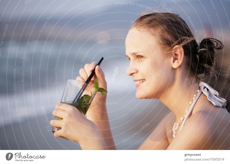 Beautiful young woman enjoying an evening cocktail sitting overlooking a tropical beach with her face turned towards the setting sun Beverage Drinking