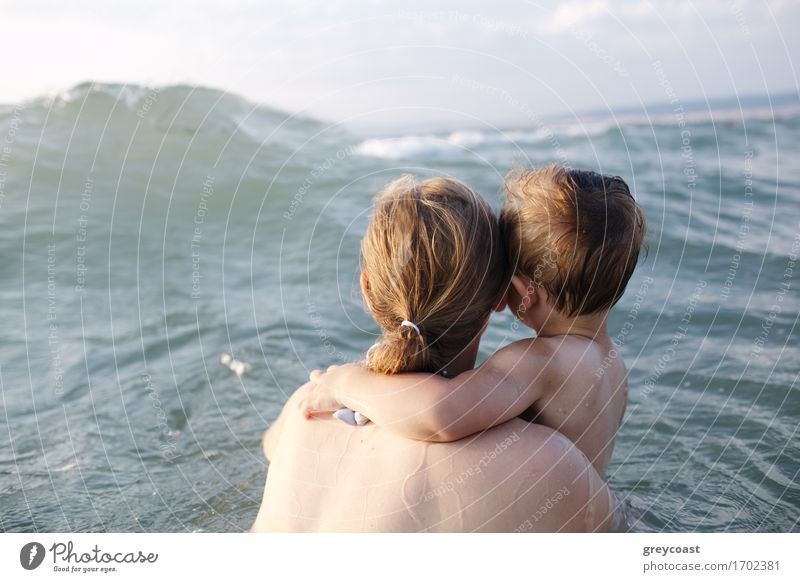 Mother swimming in the sea with her small son in her arms watching an oncoming wave, view from behind them Relaxation Vacation & Travel Summer Ocean Child Baby