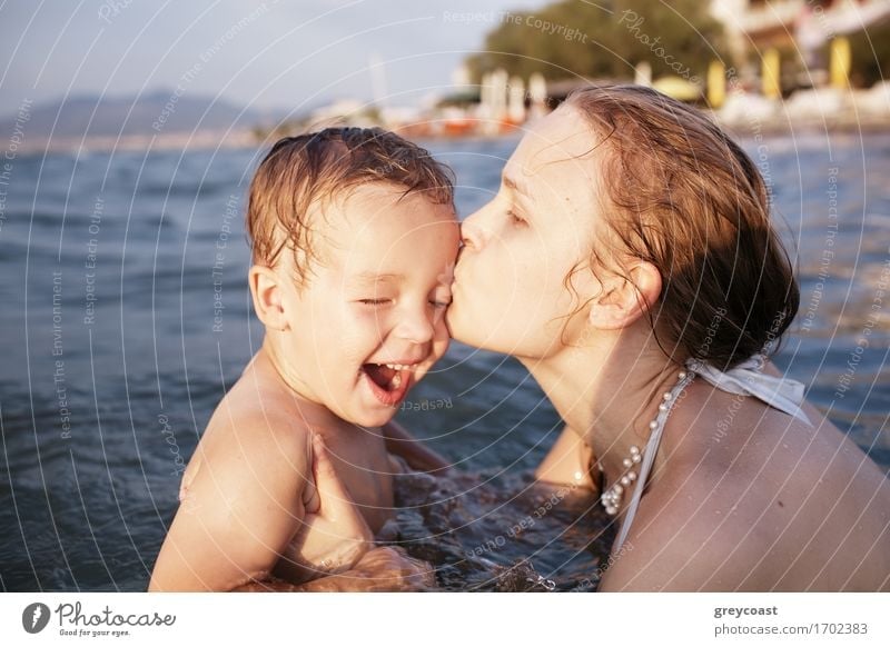 Mother kissing her young child while bathing in the sea waters during sunset Playing Vacation & Travel Sun Beach Ocean Waves Human being Child Boy (child)