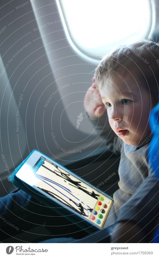 Little boy sitting in his seat during a flight and painting on a tablet computer in an airplane Leisure and hobbies Playing Computer games Vacation & Travel