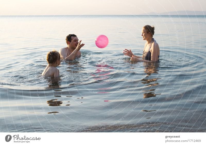 Young family enjoying the sea at sunset paddling in the shallows together playing with the ball as they enjoy their summer vacation Joy Happy