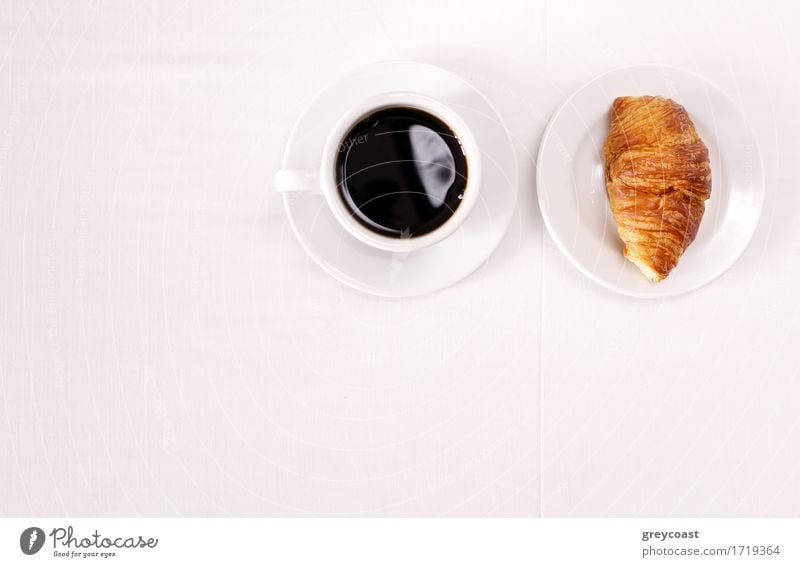Overhead view of a cup of black espresso coffee and a freshly baked croissant for breakfast. High angle close up Bread Croissant Jam Breakfast Coffee Espresso