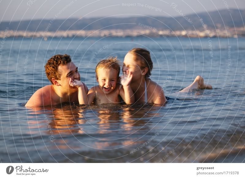 Laughing little boy flanked by his loving parents paddling together in the shallow water at the edge of the sea Lifestyle Joy Happy Beautiful Playing