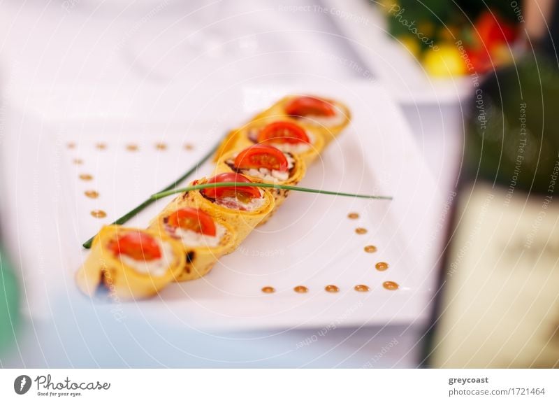 Gourmet appetizers beautifully plated at an upmarket restaurant arranged in a diagonal row on a contemporary square plate and garnished with chives. Shallow dof