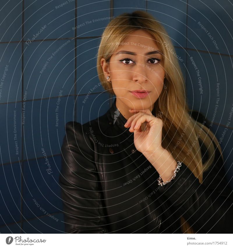 Pisa - Blonde woman in leather jacket in front of blue tiles with hand on chin looking directly into camera Feminine 1 Human being Wall (barrier)
