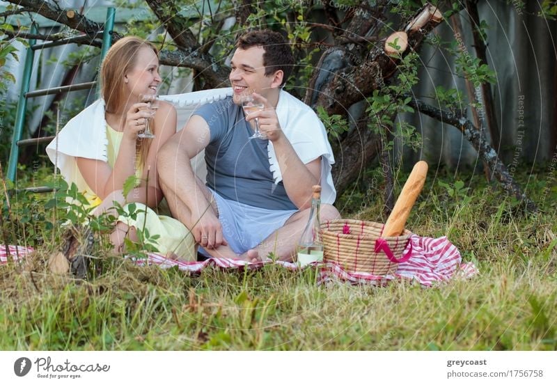 Happy young couple on picnic in the country. They sitting on the grass with glasses of wine covered with blanket. Romantic moments together Beverage