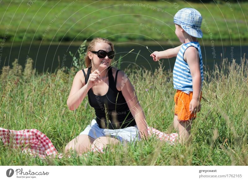 Happy mother and little son playing with grass on the meadow on the bank of a small river. Family fun outdoor Joy Relaxation Leisure and hobbies Playing Summer