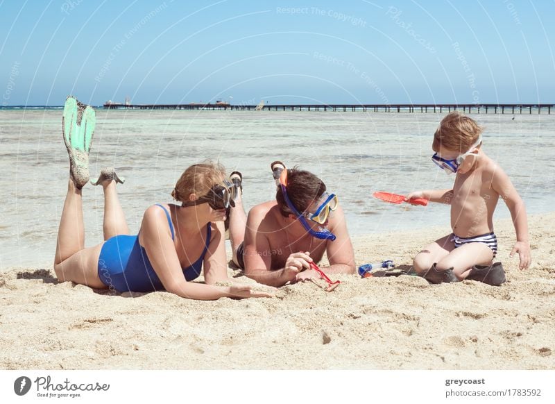 Mother, father and little son on summer vacation at the seaside, They wearing snorkels and flippers while lying and playing on the beach Joy Playing