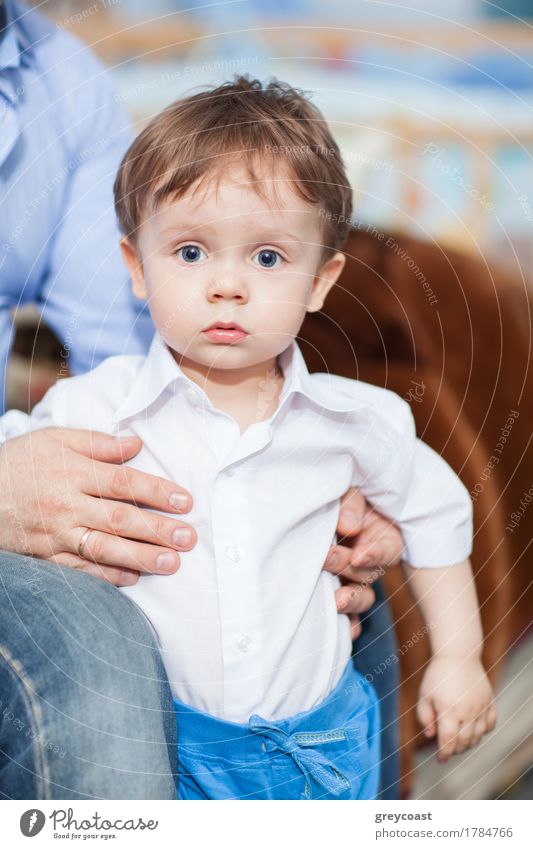 Astonished little boy stands wearing white shirt and blue trousers, father's hands support him Face Child Human being Boy (child) Man Adults Father Infancy Hand