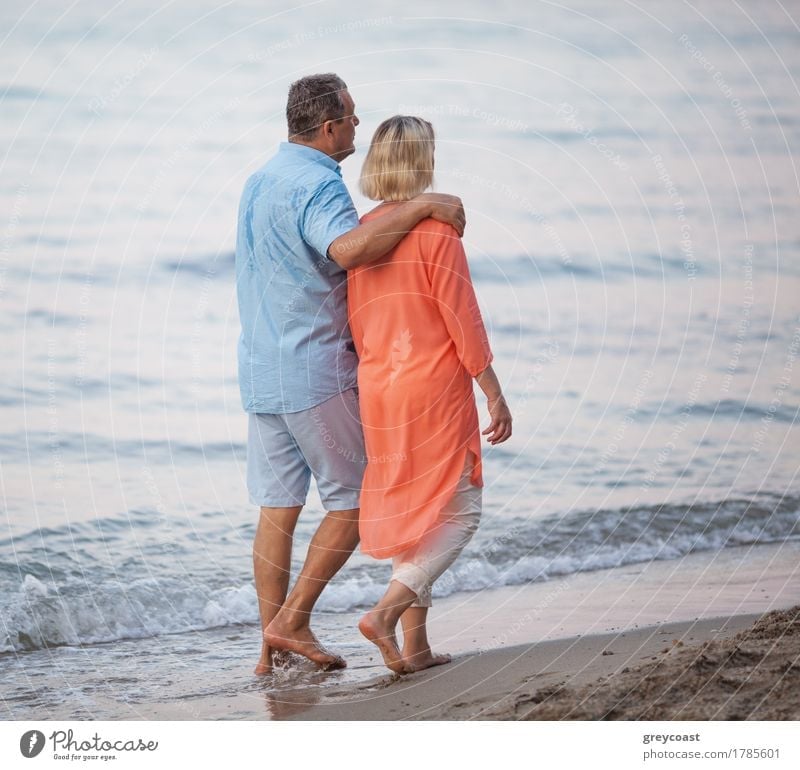 Senior couple walking together along the coast. Man embracing the woman while they having enjoyable barefoot outing on the beach Relaxation Calm