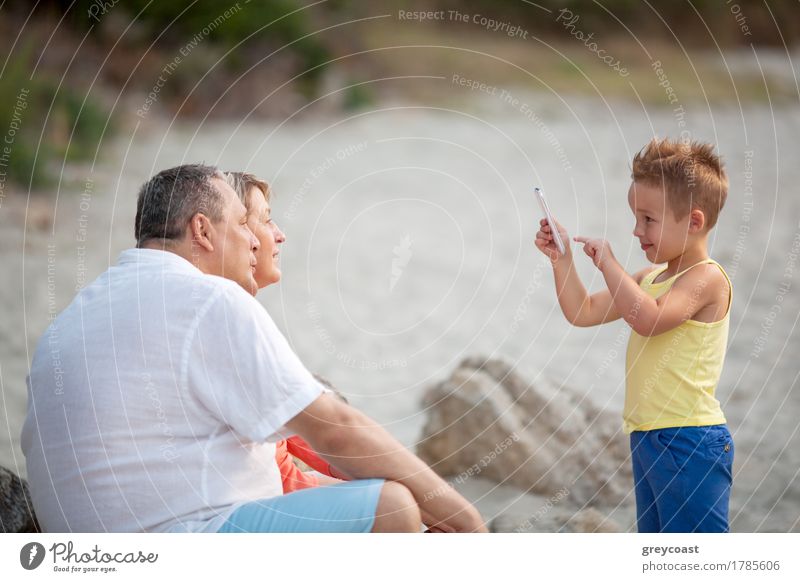 Smiling little child with smart phone taking picture of happy grandmother and grandfather. Family leisure outdoor Happy Summer Beach Child Telephone PDA Camera