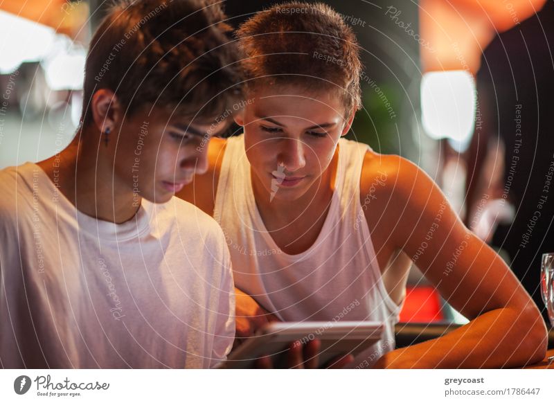 Two teenagers in white sports shirts using tablet PC in cafeteria. They looking at pad screen Leisure and hobbies Entertainment Computer Internet Human being