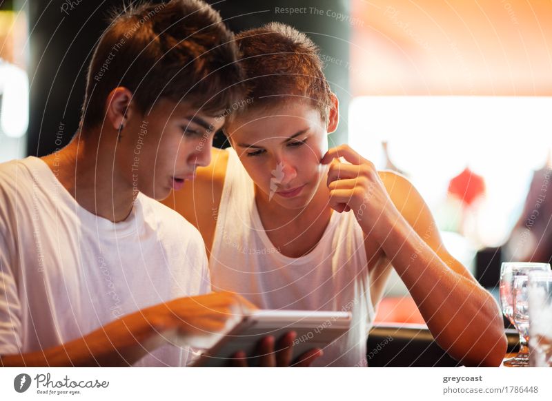 Two male teenagers surfing the internet on tablet computer while sitting in cafe. One young man pointing at screen Leisure and hobbies Entertainment Computer