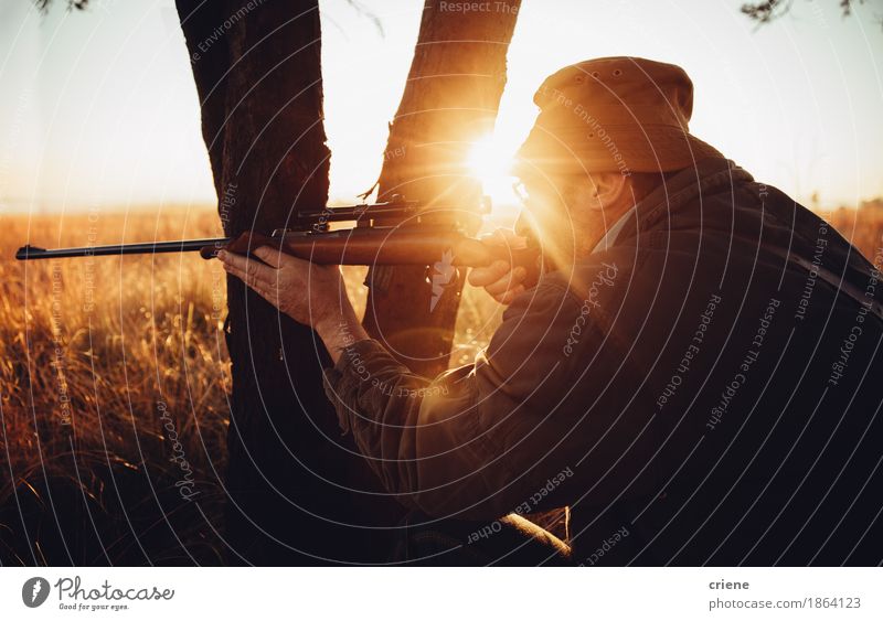 Hunter hiding behind tree on field shooting wild animal Meat Lifestyle Leisure and hobbies Hunting Sports Success Masculine Man Adults Male senior