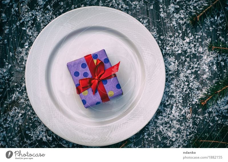 Packed gift with a red ribbon on a white plate Breakfast Lunch Dinner Crockery Plate Cutlery Snow Decoration Table Restaurant Feasts & Celebrations