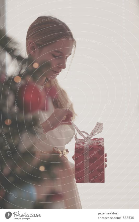 Girl unpacking Christmas gift standing behind a tree Lifestyle Feasts & Celebrations Christmas & Advent Child Human being 1 8 - 13 years Infancy Tree Dress